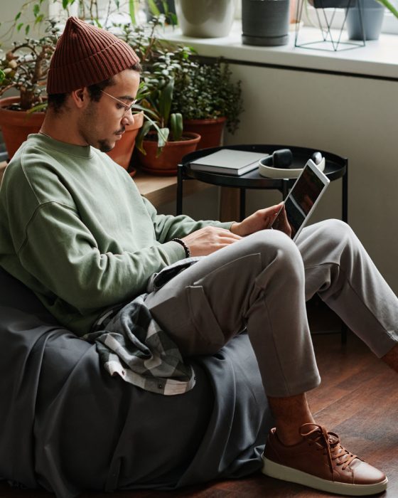 Young serious webdesigner with laptop concentrating on network Young serious webdesigner with laptop concentrating on network while sitting in comfortable armchair in office with many green plants
